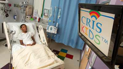 Young boy laying in a hospital bed with a CRISKids logo showing on the TV.