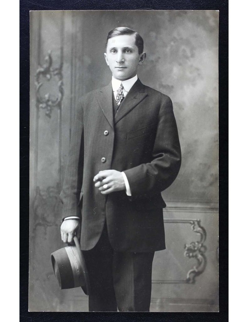a black and white photo of samuel benjamin yaffo wear a suit and tie and holding a hat in is right hand with a ciagr in his left hand